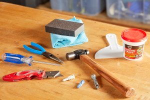 Tools and materials such as hammers, pliers, drywall spackle all laid on table.