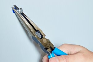 Woman uses needle-nose pliers to pull a screw out of a drywall anchor.