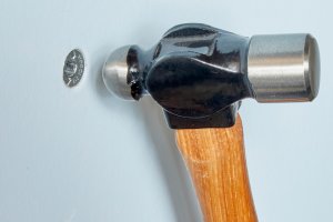 Using a ball peen hammer to recess a drywall anchor in the wall.