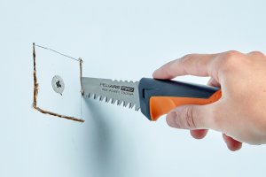 Woman uses a small saw to cut a drywall anchor out of a wall.