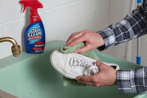 Woman rubs stain remover onto white sneakers with a cloth.
