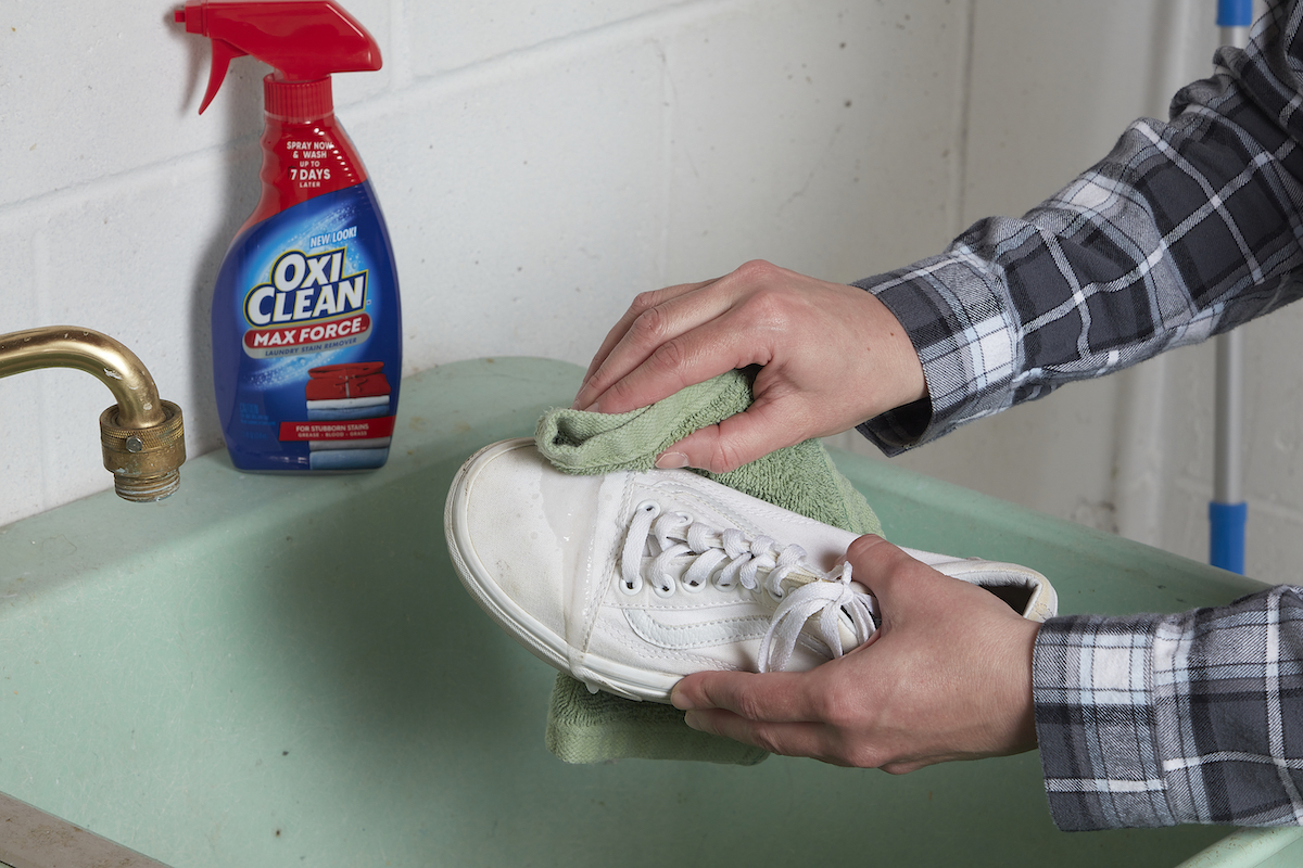 Woman rubs stain remover onto white sneakers with a cloth.