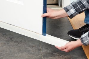 Woman installs a white door sweep underneath an exterior door.