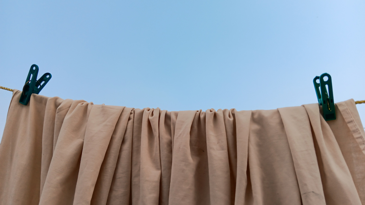 A beige curtain is hanging onto a clothesline outside with two clips.