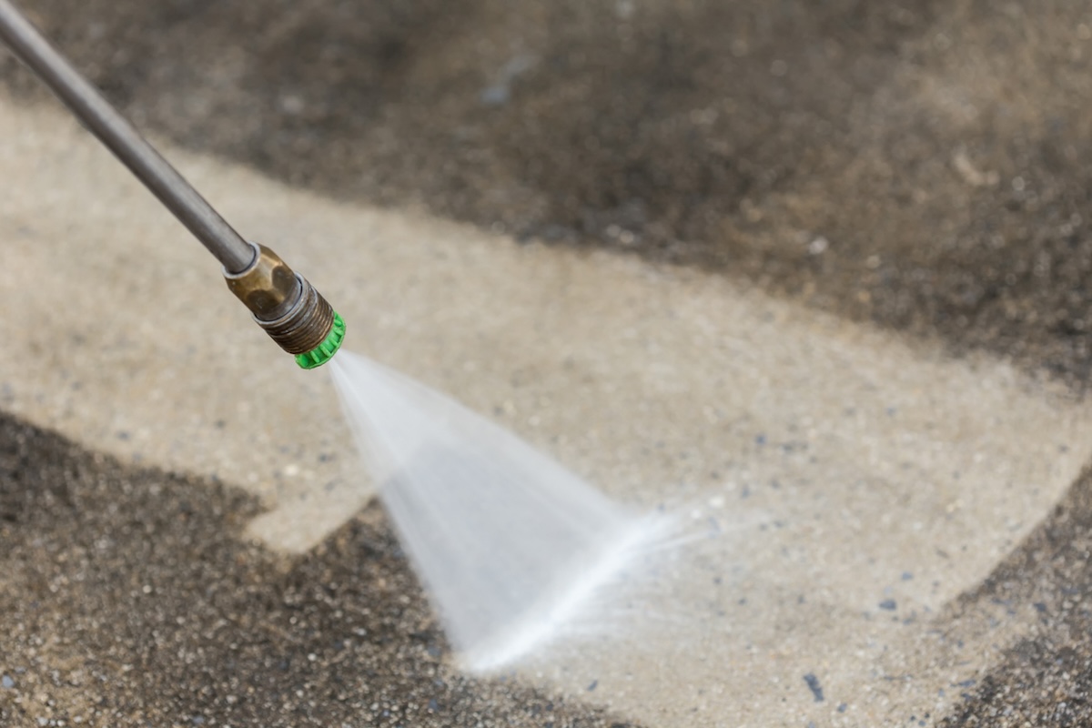 A person cleaning a dirty garage floor with a degreaser and pressure washer.