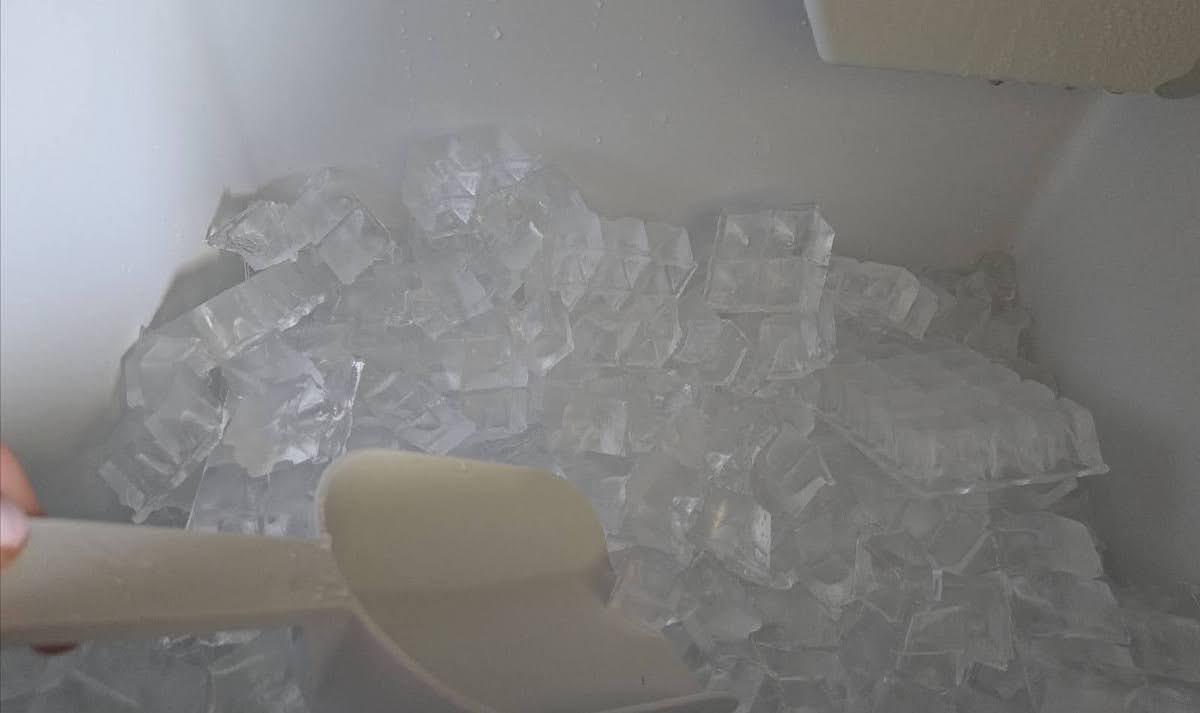 A person is collecting ice in a commercial ice maker with a plastic hand scoop.