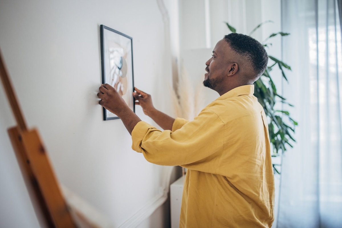 Man hangs a framed picture on living room wall.