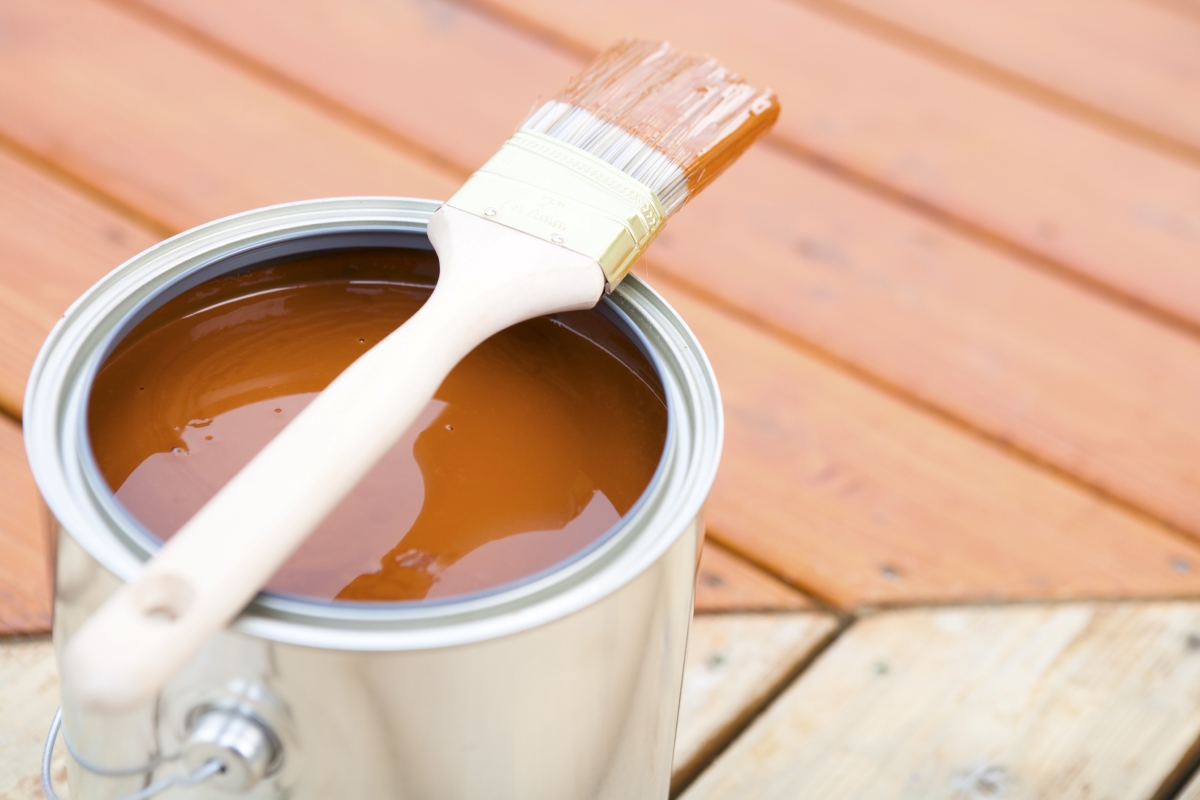 A paintbrush is sitting on top of a tin can full of wooden stain.