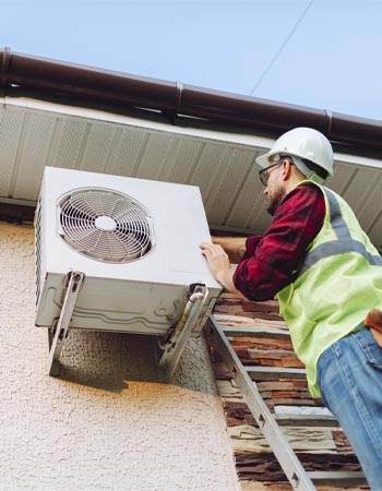 A worker in a hard hat and a safety vest climbs a ladder to repair an AC unit. 