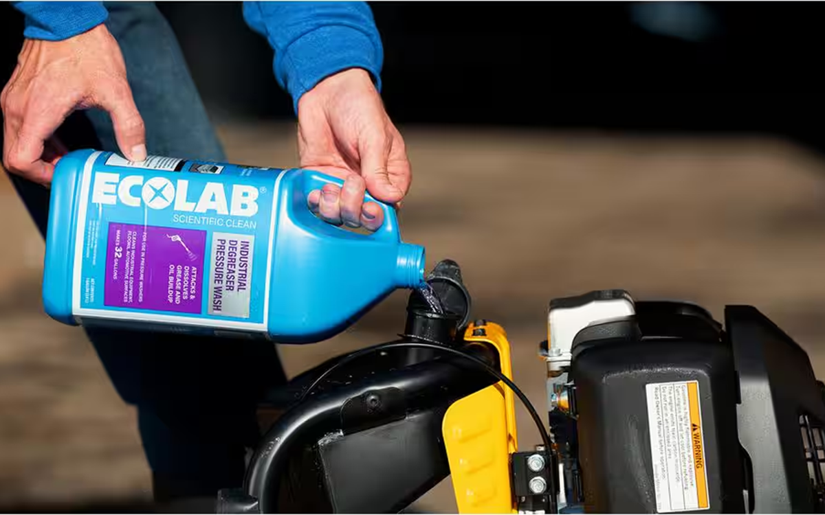 A person filling a pressure washer with Ecolab industrial degreaser solution for cleaning concrete.