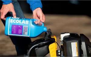 A person filling a pressure washer with Ecolab industrial degreaser solution for cleaning concrete.