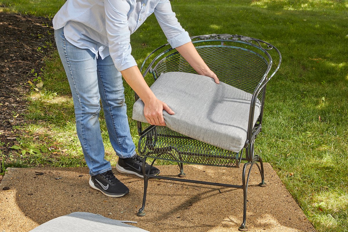 Woman replaces a grey patio cushion on an iron outdoor chair.