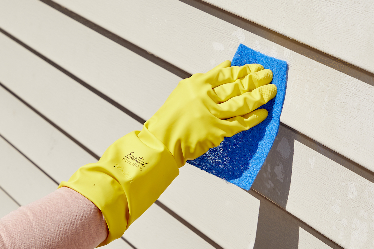 Woman wearing yellow rubber gloves uses a scrub pad to remove stains from vinyl siding.