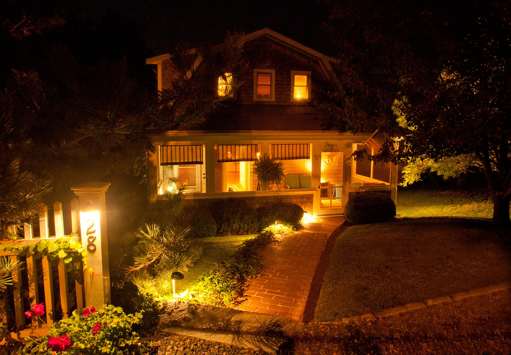 A cozy two story house with screened porch illuminated at night by path lights