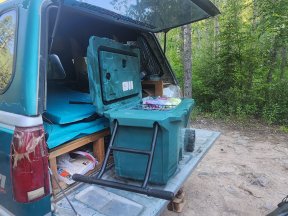 Wheeled teal Brumate cooler with lid open and lots of food inside in the back of a truck