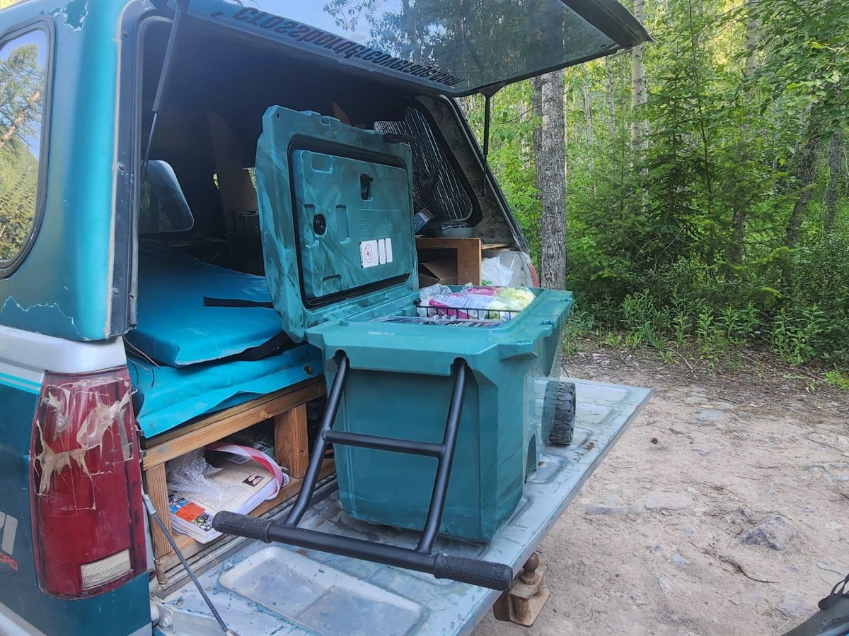 Wheeled teal Brumate cooler with lid open and lots of food inside in the back of a truck