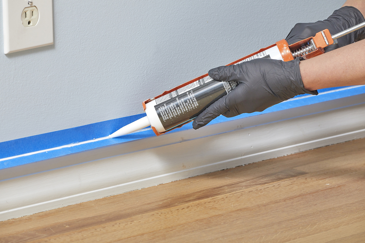 Woman applies caulk between rows of painter's tape with a caulk gun.
