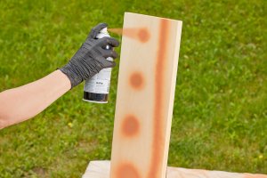 Woman tests spray paint on a piece of wood.