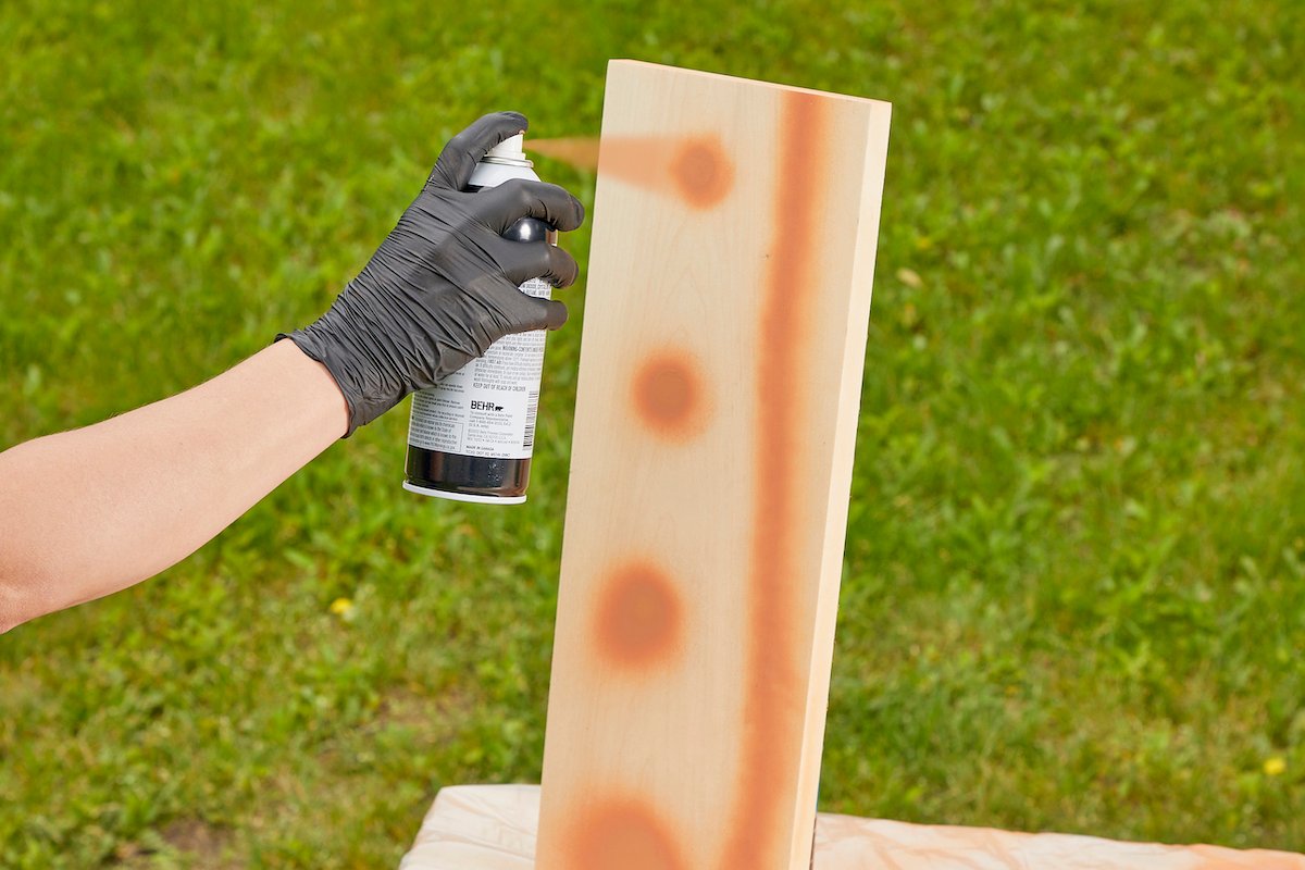 Woman tests spray paint on a piece of wood.