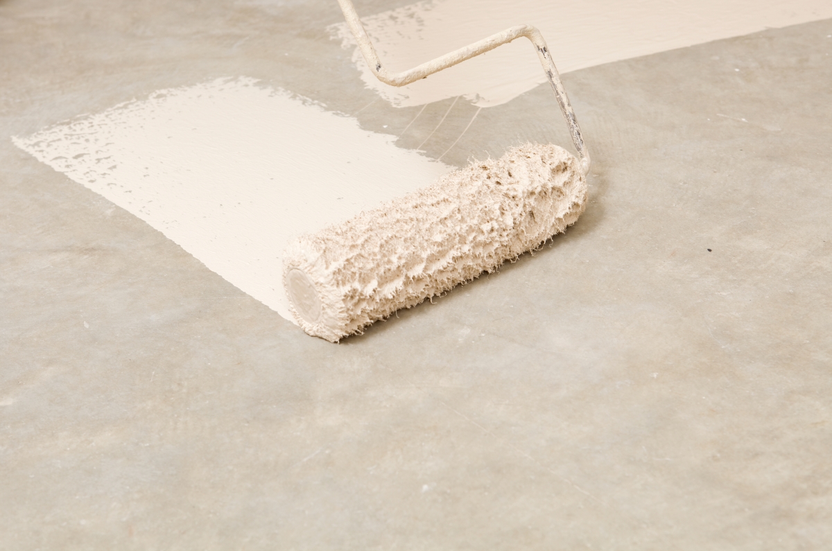Using a paint roller to paint a concrete floor white.