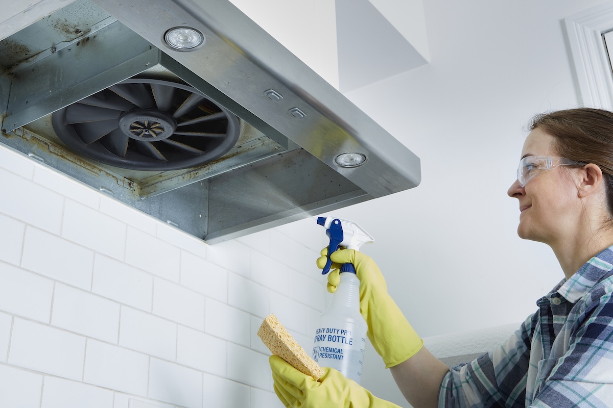 Woman sprays a greasy range hood with a cleaning solution.