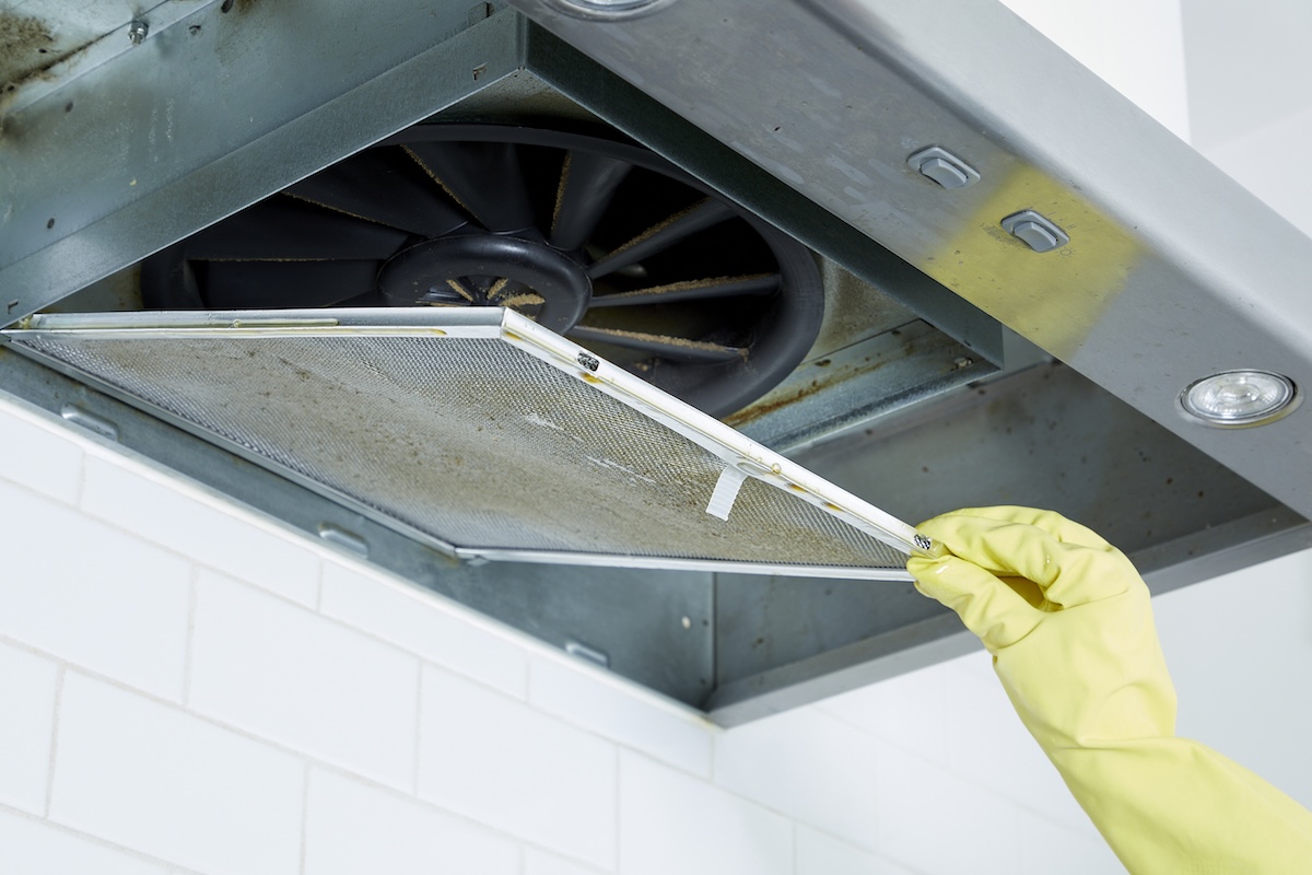 Woman begins to remove the range hood filter from a range hood.