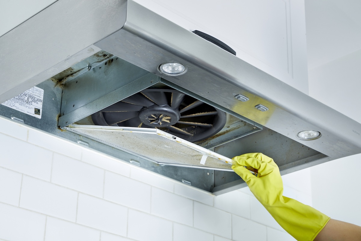 Woman wearing rubber gloves removes a range hood filter from a range hood.