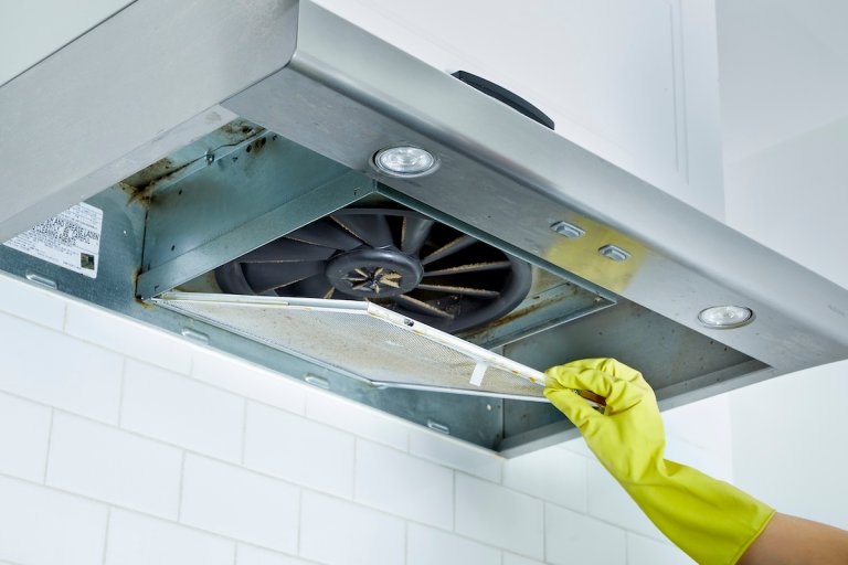 Woman wearing rubber gloves removes a range hood filter from a range hood.