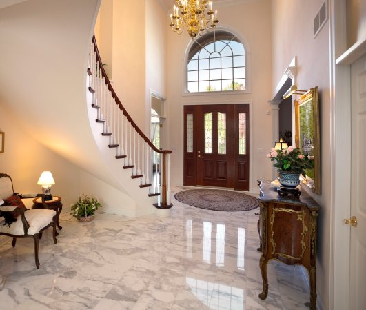 Grand foyer with curved staircase, brown wooden door, and chandelier.