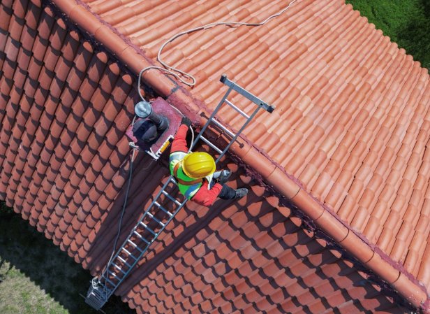 A professional contractor is on the roof working near the exhaust fan.