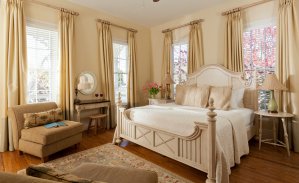 A beautiful guest bedroom replete with windows, two easy chairs, bedside tables, and a console table that doubles as a desk.