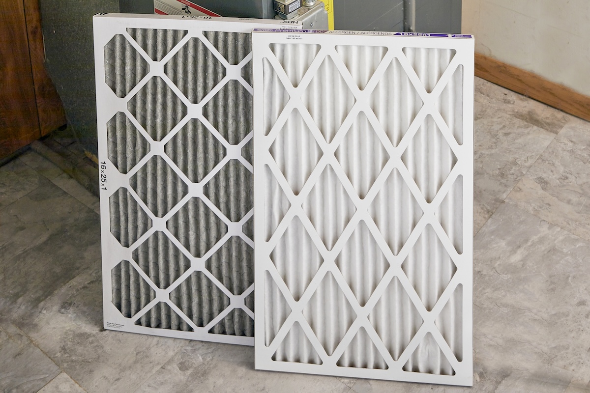 An old and new furnace filter side by side next to the furnace.