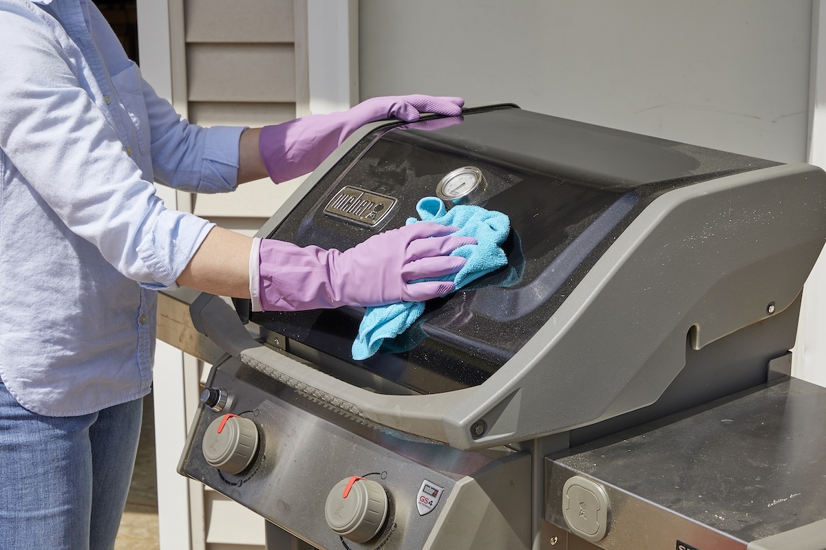 Woman wearing rubber gloves wipes the exterior of a grill with a cloth.