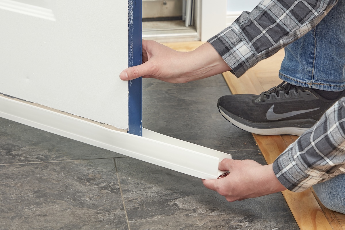 Woman slides door sweep weatherstripping under a front door.
