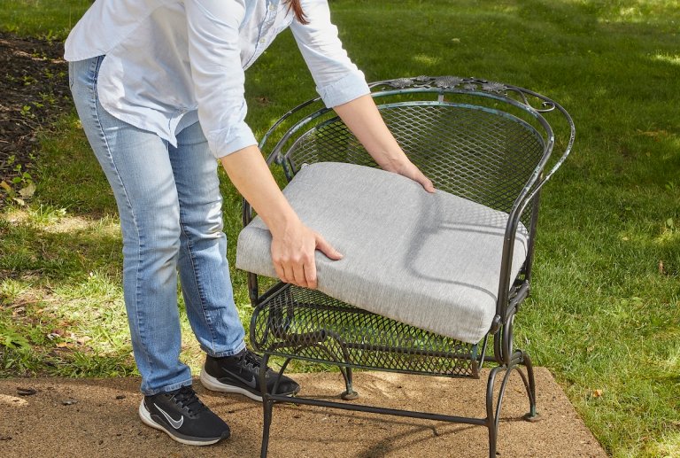 Woman removes cushion from metal patio chair.