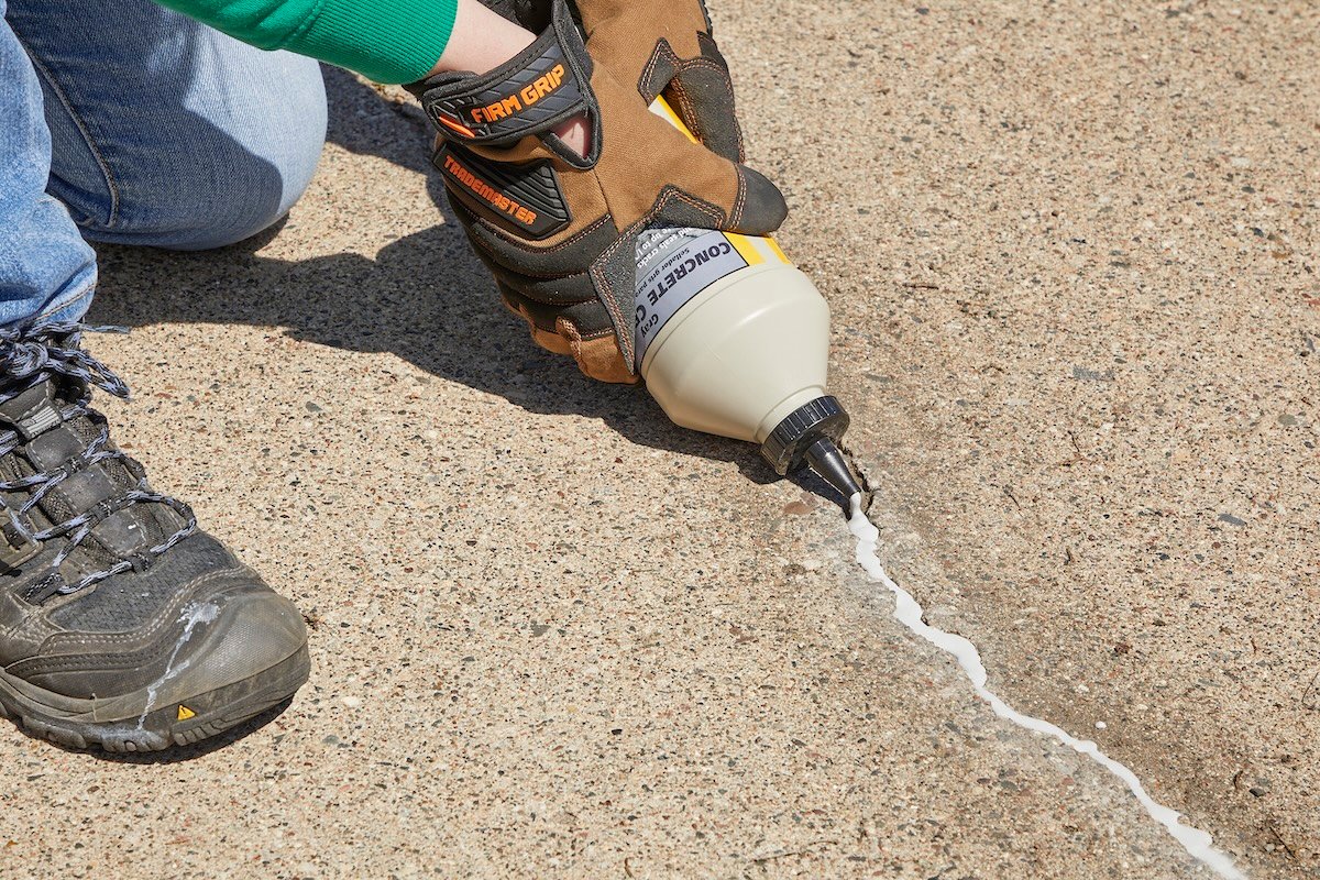 Woman fills crack in concrete driveway with concrete filler.