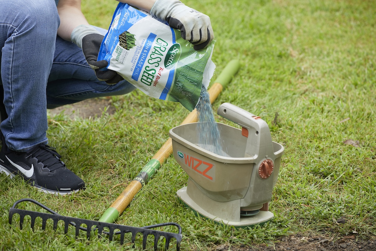 Person pours Scotts grass seed into a seed spreader.