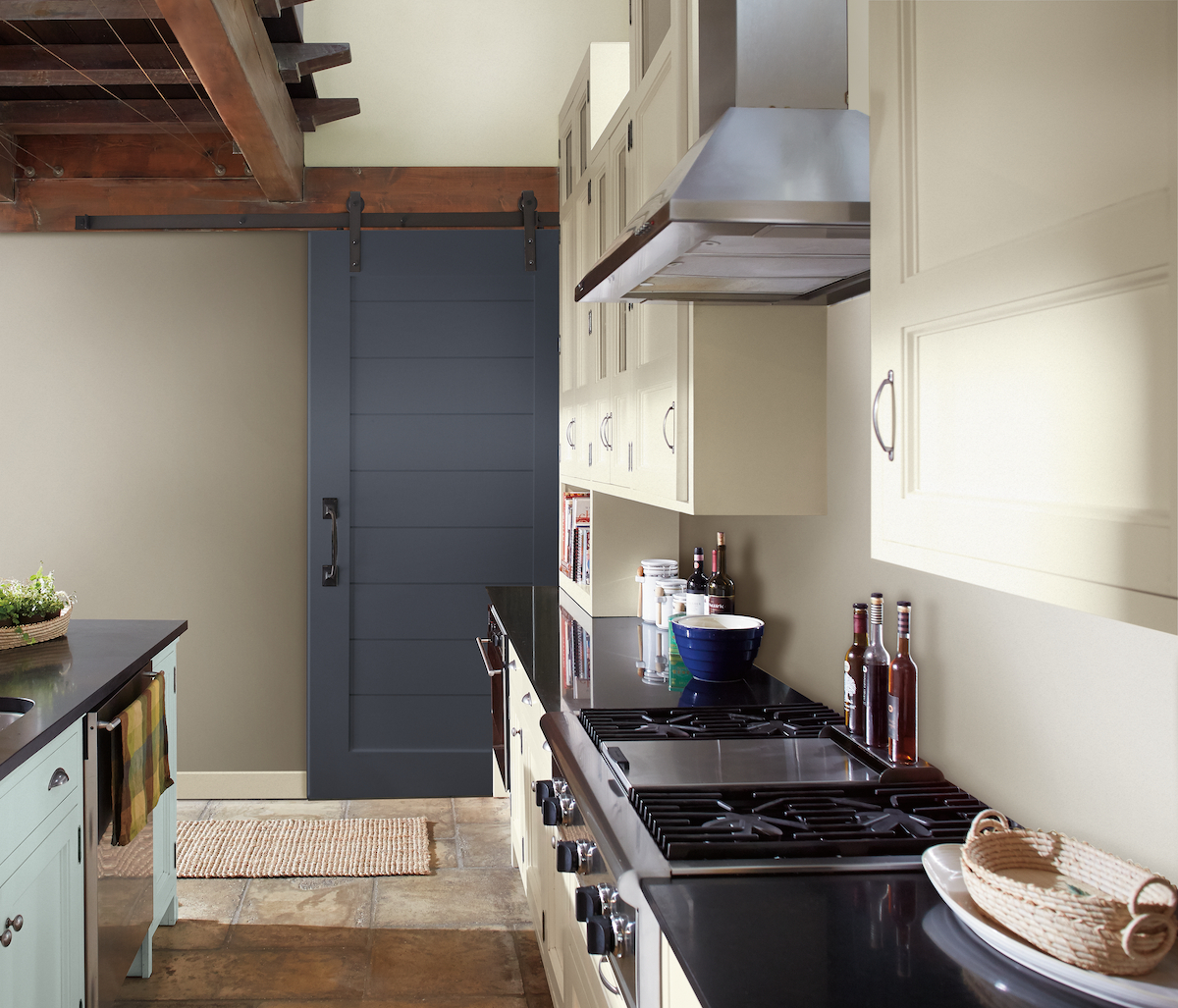 A galley kitchen is mostly cream-colored with a a large navy blue barn door.