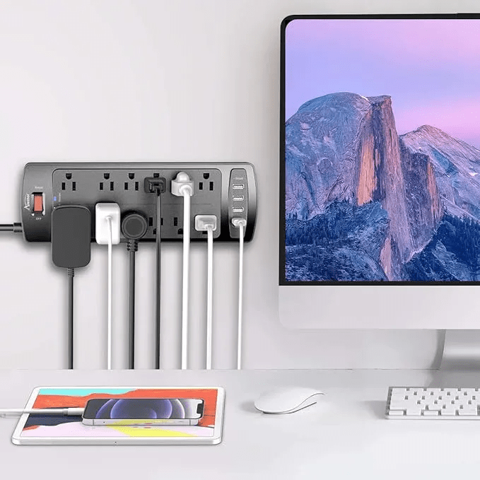 Power Strip, ALESTOR Surge Protector with 12 Outlets and 4 USB Ports, 6 Feet Extension Cord (1875W/15A), 2700 Joules, ETL Listed, Black plugged into wall next to computer monitor.