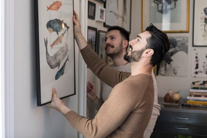 Two men hanging artwork on the wall in a home.