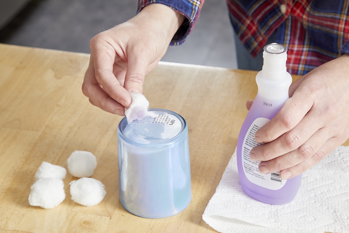 A person removing glue from bottom of candle jar using nail polish remover.