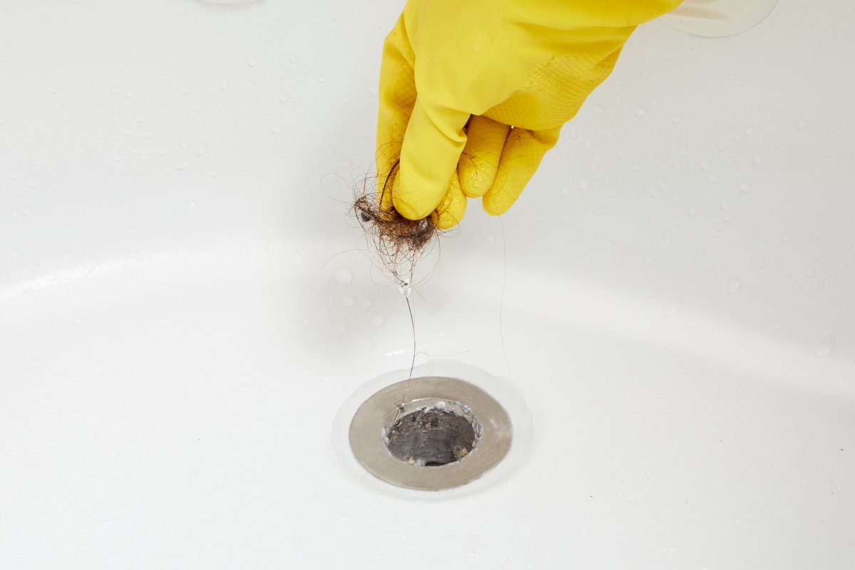 A person pulling a clog out of a shower drain.