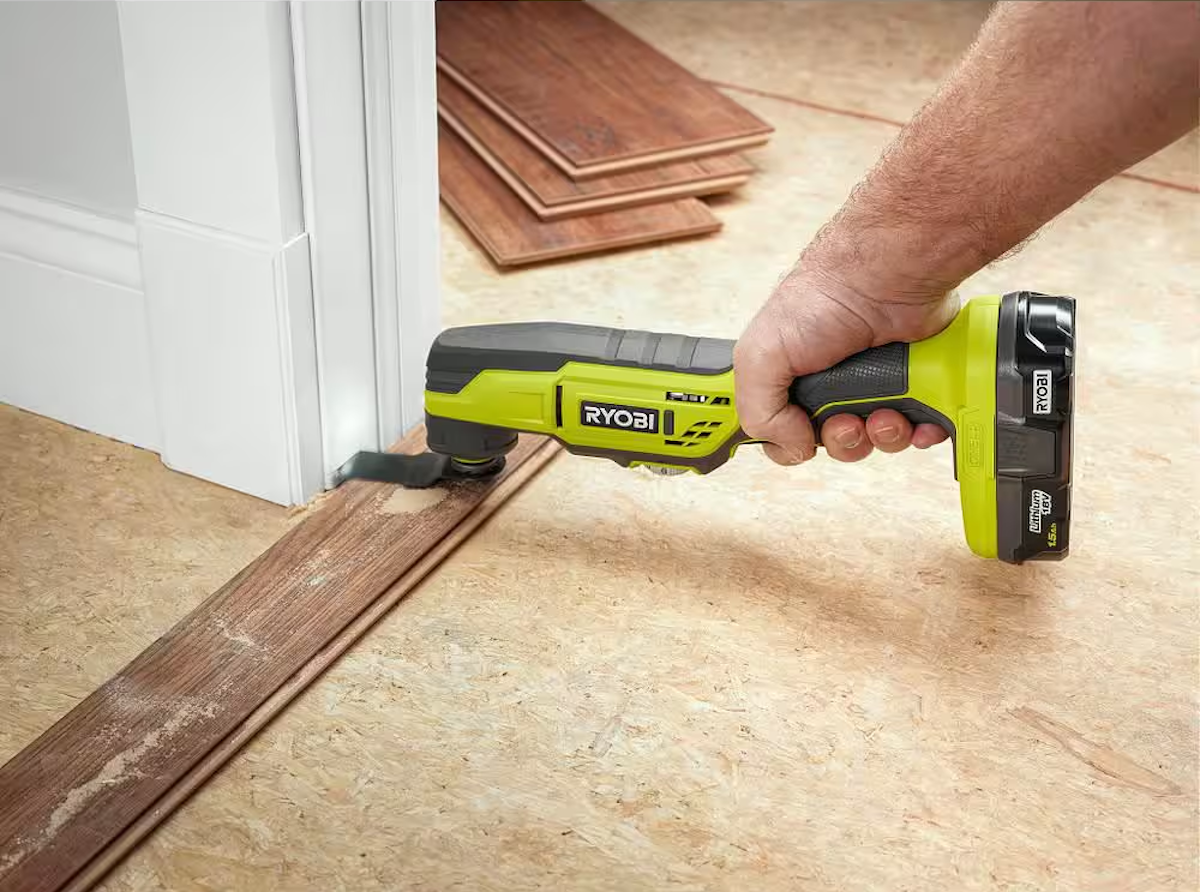 A person using an oscillating tool to cut baseboards for new flooring.