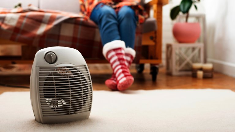 Electric fan heater on the floor in living room with human sitting on the sofa at background