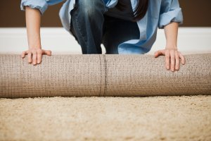 Direct image of woman (head not shown) unrolling a large carpet.