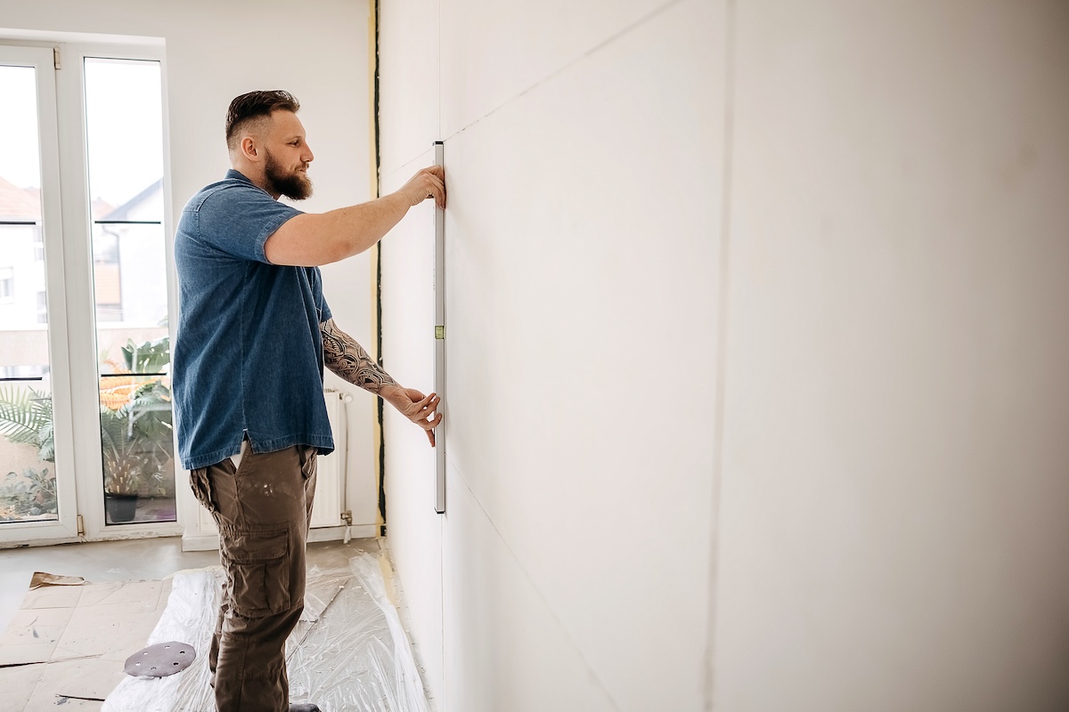 A man in a denim shirt with a beard finds studs in a wall.