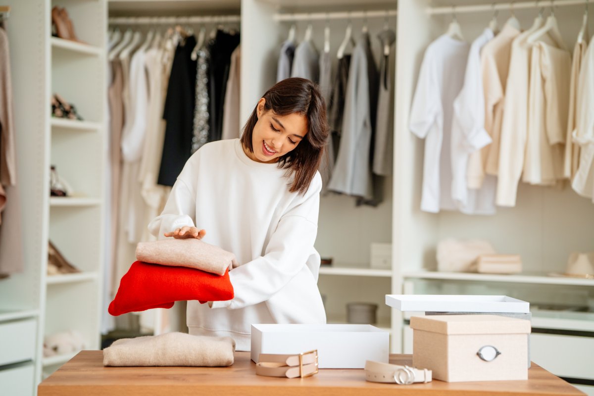 Brunette woman packing and stacking clothes items into the boxes in a walk-in closet.