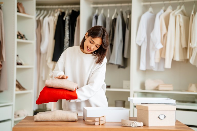 Brunette woman packing and stacking clothes items into the boxes in a walk-in closet.