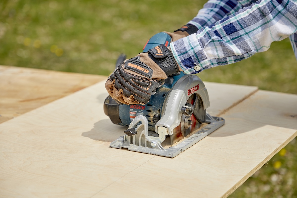 A DIYer using a circular saw to rip plywood outdoors on sawhorses.