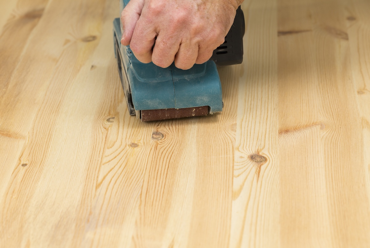 A DIYer sanding a hardwood floor with a belt sander.